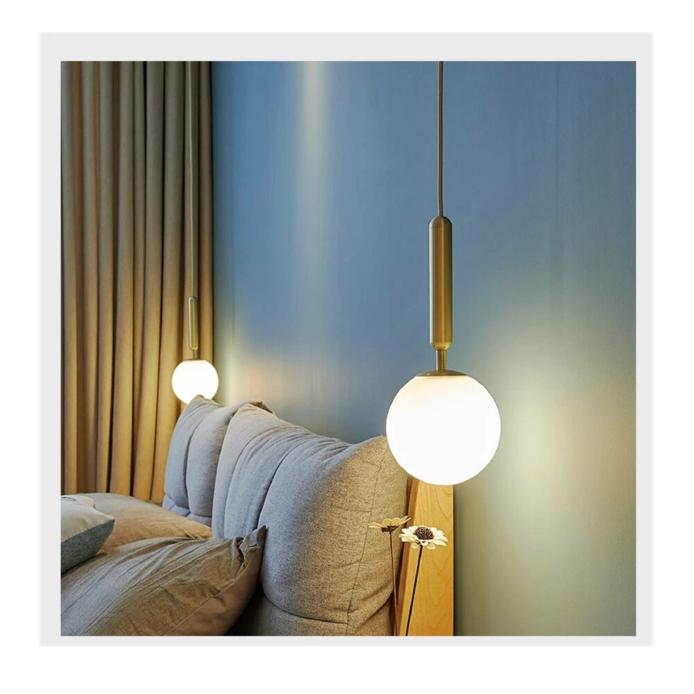 Photo de deux lustres boule dorés allumés de part et d'autre d'un canapé dans une pièce au mur gris vert et un e tenture camel au fond