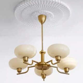 Photo d'un lustre art déco doré à cinq têtes au verre jaune suspendu au milieu d'une moulure style ancien sur un plafond blanc