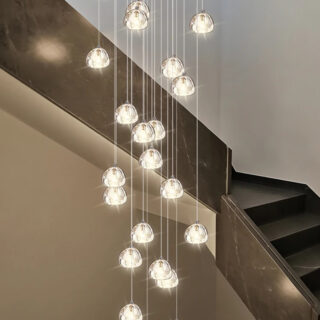 Photo d'un lustre d'escalier à boules de cristal lumineuses sur des filins dans une descente d'escalier beige et marron
